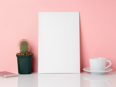 Blank white frame and plant cactus, cup of coffee or tea on a white table against the pink wall with copy space. Mockup with copy space.