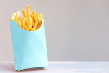 French fries in a blue carton box on the white table and grey background