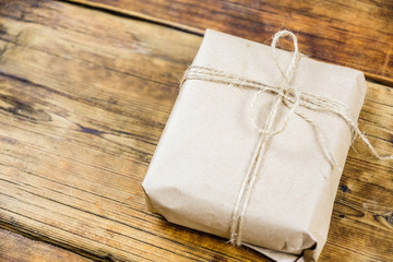 Close-up gift wrapped kraft paper on wooden background. Left on photo.