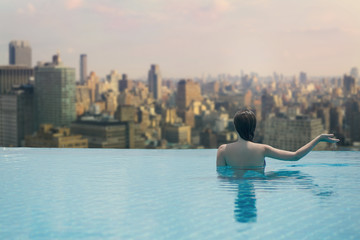 Young female in the pool on the roof on the background of skyscrapers of New York City, Manhattan