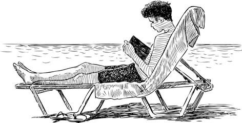 Fototapeta premium A teen boy reads a book on a beach