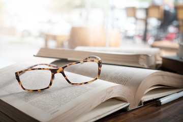 Glasses on opening book in library or cafe.