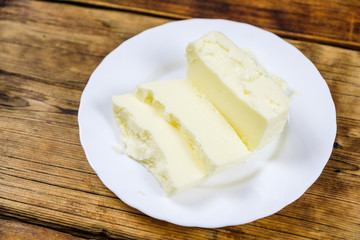 Fresh farm piece of butter on a white plate on wooden background. Farm products.