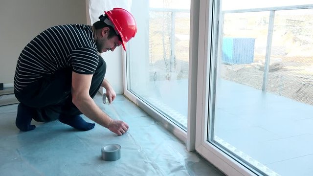 caucasian worker lay polyethylene film on floor.