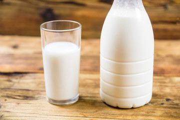 Bottle of fresh farm milk and glass of milk on wooden background. Side view.