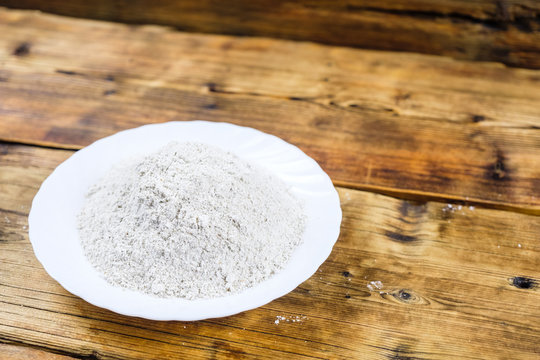 Close-up heap with wheat flour coarse in white plate on wooden background. Left on the photo