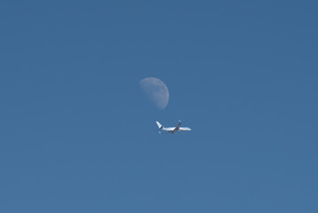 travel image of charter airplane flying in front of moon during day