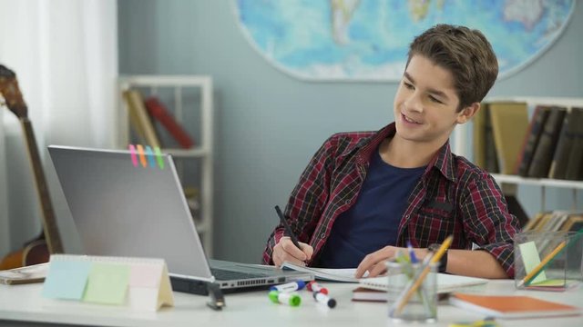 Happy cunning teenager copying homework assignment from internet, cheating
