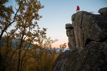 Back view of young man doing parkour standing on rock and looking at landscape in sunset lights.  