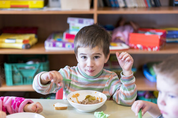 A boy at the age of 5 years eating soup in the kindergarten.