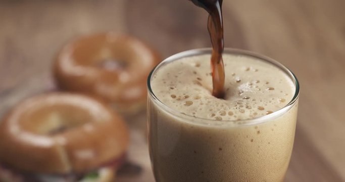 Slow motion stout beer poring into glass with bagels on background