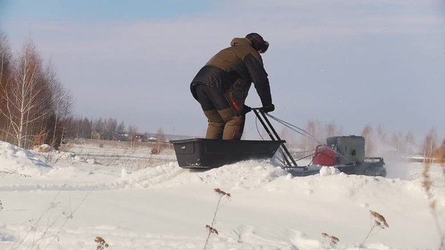 Man in winter clothes overcoming high snow on a mini snowmobile