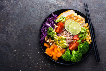 Buddha bowl dish with chicken fillet, brown rice, avocado, pepper, tomato, broccoli, red cabbage, chickpea, fresh lettuce salad, pine nuts and walnuts. Healthy balanced eating. Top view