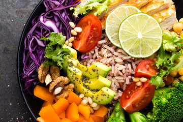 Buddha bowl dish with chicken fillet, brown rice, avocado, pepper, tomato, broccoli, red cabbage, chickpea, fresh lettuce salad, pine nuts and walnuts. Healthy balanced eating. Top view