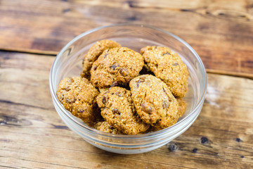 Homemade oatmeal cookies with raisins in glass plate on wooden background. Top view.