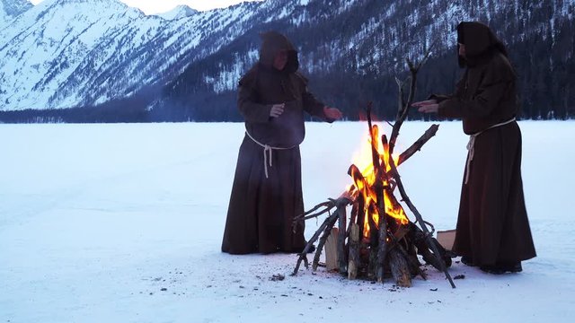 monks franciscans are warming near fire in winter