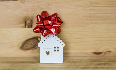 Small White House Model with Red Ribbon  On Wooden Background