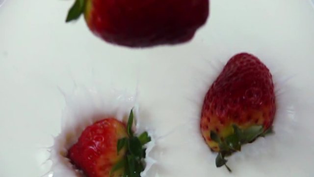 Fresh strawberries falling into cream in slow motion