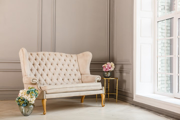 Vintage sofa of soft pink color decorated with flowers and greens stands in a classic room