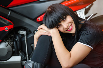Plakat A biker girl in black clothes on a sports motorcycle posing while sitting in the city