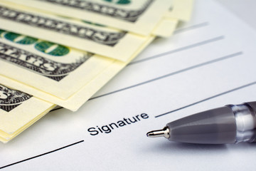 pen laying over a contract waiting to be signed money dollars