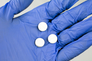 white pills in hand blue medical glove close up, selective focus, blurred neutral background