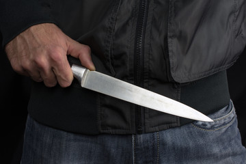 big knife in young man hand of a  black jacket clenched fist close up, selective focus , blurred...