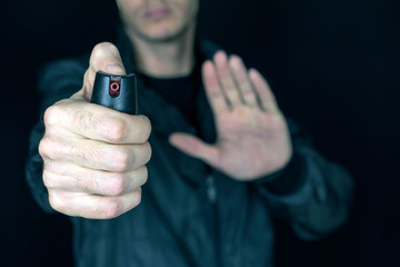 pepper gas in the hand of a young man in a black jacket CS spray self-defense Tear gas concept, close up, selective focus , blurred dark background