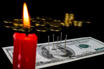 needles stuck in a dollar bill voodoo ritual, red candle, smoke and fire, gold coins, close up...