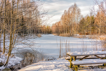 A resting place in winter at an ice-covered and snow-covered pond in a natural park in Handen just outside Stockholm, Sweden.
