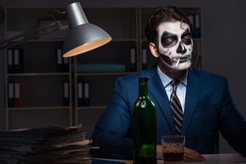 Businessman with scary face mask working late in office