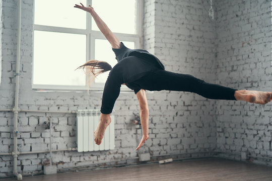 The young attractive modern ballet dancer in black jacket jumping over urban background.