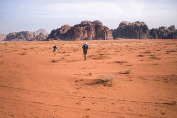 Fototapeta na wymiar Two hikers in a sand desert. Tourist friends in Jordan natural park Wadi Rum.Group of backpackers walking on the road. Natural background.