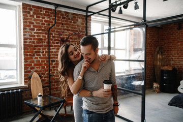 Young stylish hipsters couple. guy and girl in love hugging together. Indoors. Portrait. interior in style the loft. lifestyle moments at home. The man and the woman have coffee and communicate