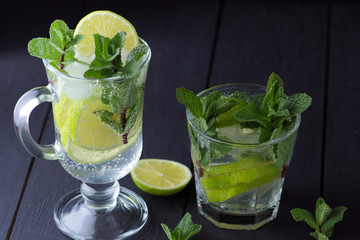 Mojito on a dark background, summer cocktail with lime, refreshing drink with lemon, fresh mint for cocktail, celebratory drink with ice, vegan, copy space, minimalist cocktail
