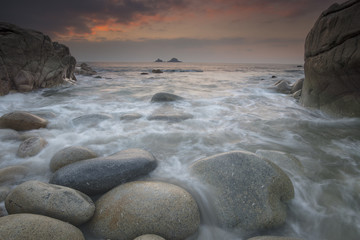 Fototapeta na wymiar Boulders on Porth Nanven beach looking towards the Brisons at sunset Cot Valley Cornwall