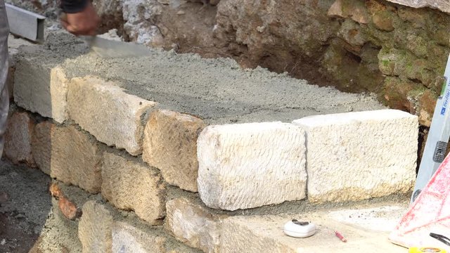Construction worker builds brick wall, closeup view at construction site. Builder corrects the block by hammer