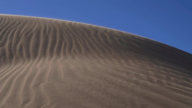 The wind blowing sand across a desert sand dune