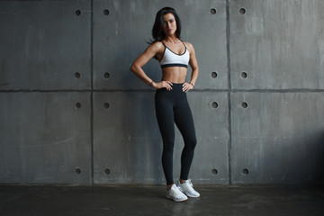 young adult girl stand near concrete wall in gym in sportswear