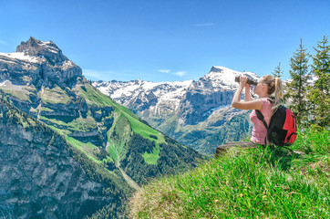 girl traveler looks through binoculars, against a backdrop of mountain peaks, admires the nature and mountain landscapes of Switzerland, the Engelberg resort
