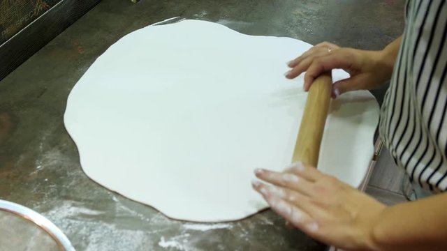 Woman rolling sugar mastic with rolling pin on table for making dessert