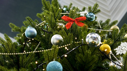 Decorated Christmas tree on blurred, sparkling and fairy background. New Year's toys hang on the Christmas tree. Classic christmas and New Year decorated interior room with presents and New year tree.