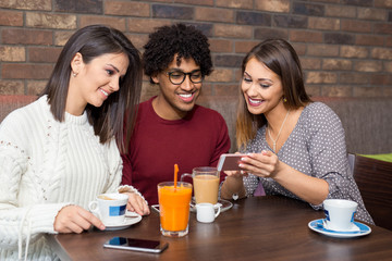 Group of friends having fun in a restaurant cafe while playing on a smartphone