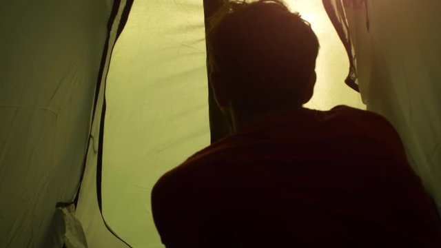 Young man backpacker exits camping tent in front of roman aqueduct arches in parco degli acquedotti park ruins in rome at sunset sticks in ground shot from inside tent camera slow motion pov
