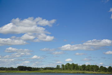 Puffy white clouds against a blue sky over the river