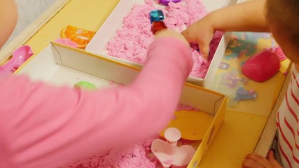 Children playing with pink play sand/magic sand Close-up/closeup shot of two children/kids/babies/sisters playing with pink play/magic/moon/space sand