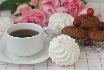 White marshmallows, chocolate muffins, a cup of coffee and roses. Close-up