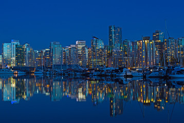 Fototapeta na wymiar Vancouver city skyline at night in British Columbia, Canada. Modern building and waterfront marina with reflection in calm waters.