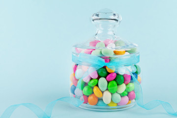 Glass jar stuffed with colorful candy against blue background. Gifts for Birthday or Happy Easter.