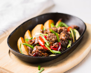 Grilled steak, baked potatoes and vegetables.  Beef meat stewed with potatoes, carrots, sweet red peppers, green onions and spices in frying pan on white wooden table.